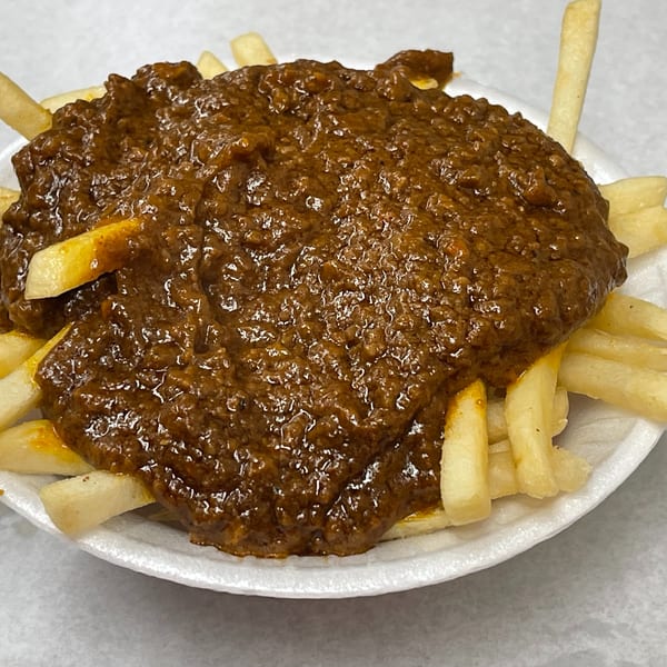 A white bowl filled with golden french fries generously topped with a thick, rich brown chili.