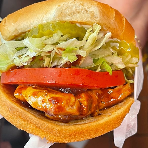 Close-up of a BBQ chicken sandwich with lettuce, tomato, and pickles on a bun.
