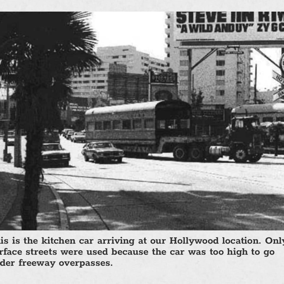 Black and white photo of a large kitchen car being towed down a city street.