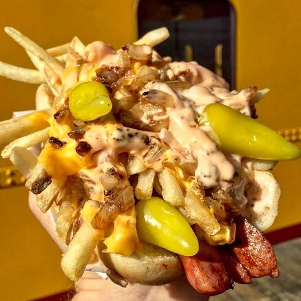 Loaded hot dog with fries, cheese, grilled onions, sauce, and pickled peppers.