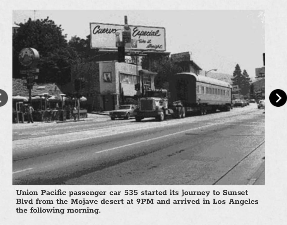 Black and white photo of a train car on a flatbed truck driving down a street.