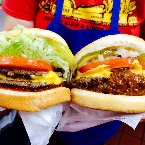 Two hands hold a double cheeseburger with lettuce and tomato, and a chili cheeseburger with pickles.