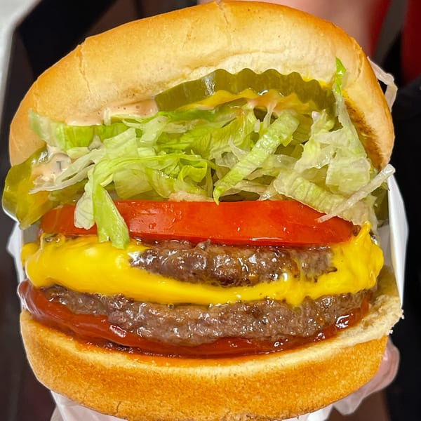 Close-up of a double cheeseburger with lettuce, tomato, pickles, and special sauce on a bun.