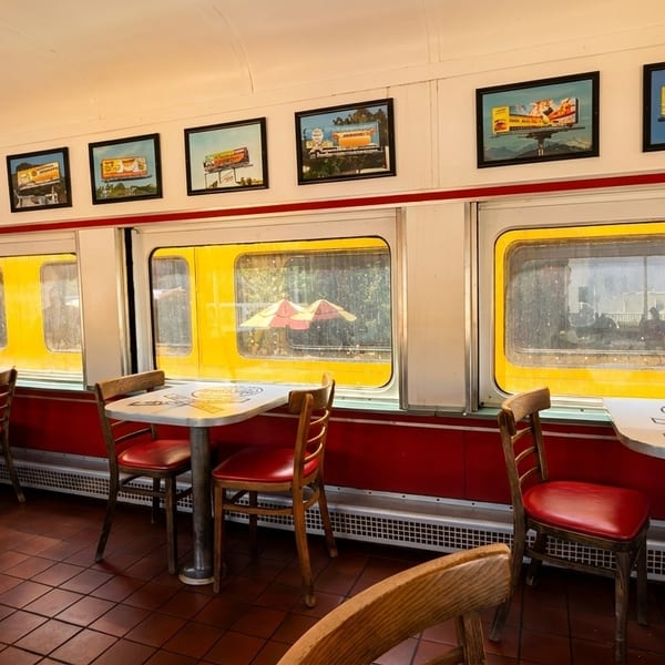 Interior of a diner-style restaurant with red booths, small tables, and framed pictures on the walls.