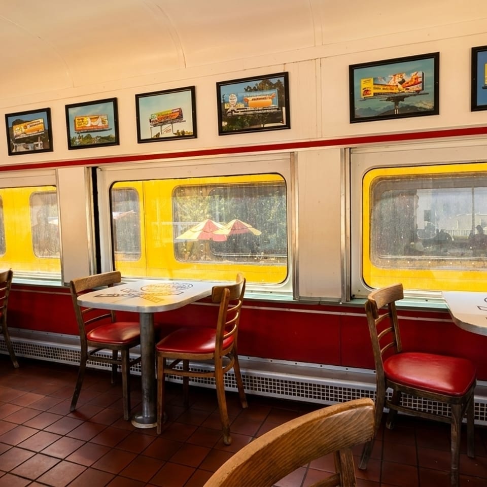 Interior of a diner-style restaurant with red booths, small tables, and framed pictures on the walls.