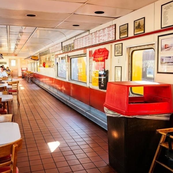 Diners seated at tables inside a vintage train car restaurant with red and white decor.