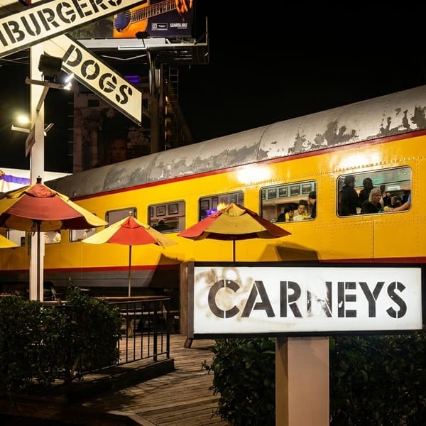Carney's restaurant at night, a yellow train car with patrons inside, and outdoor seating with umbrellas.