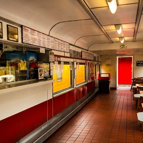 Interior of a vintage diner car with red and white counters, wooden tables, and a bright red door.