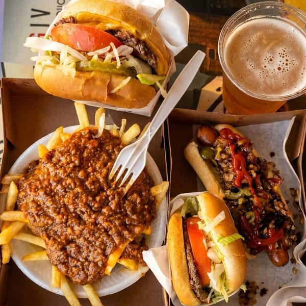 Carney's chili cheese fries, hot dogs, cheeseburger, and beer on a train car table.