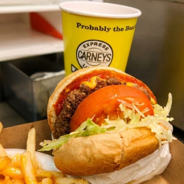 Carney's burger with tomato and lettuce, cheese fries, and a yellow Carney's cup.