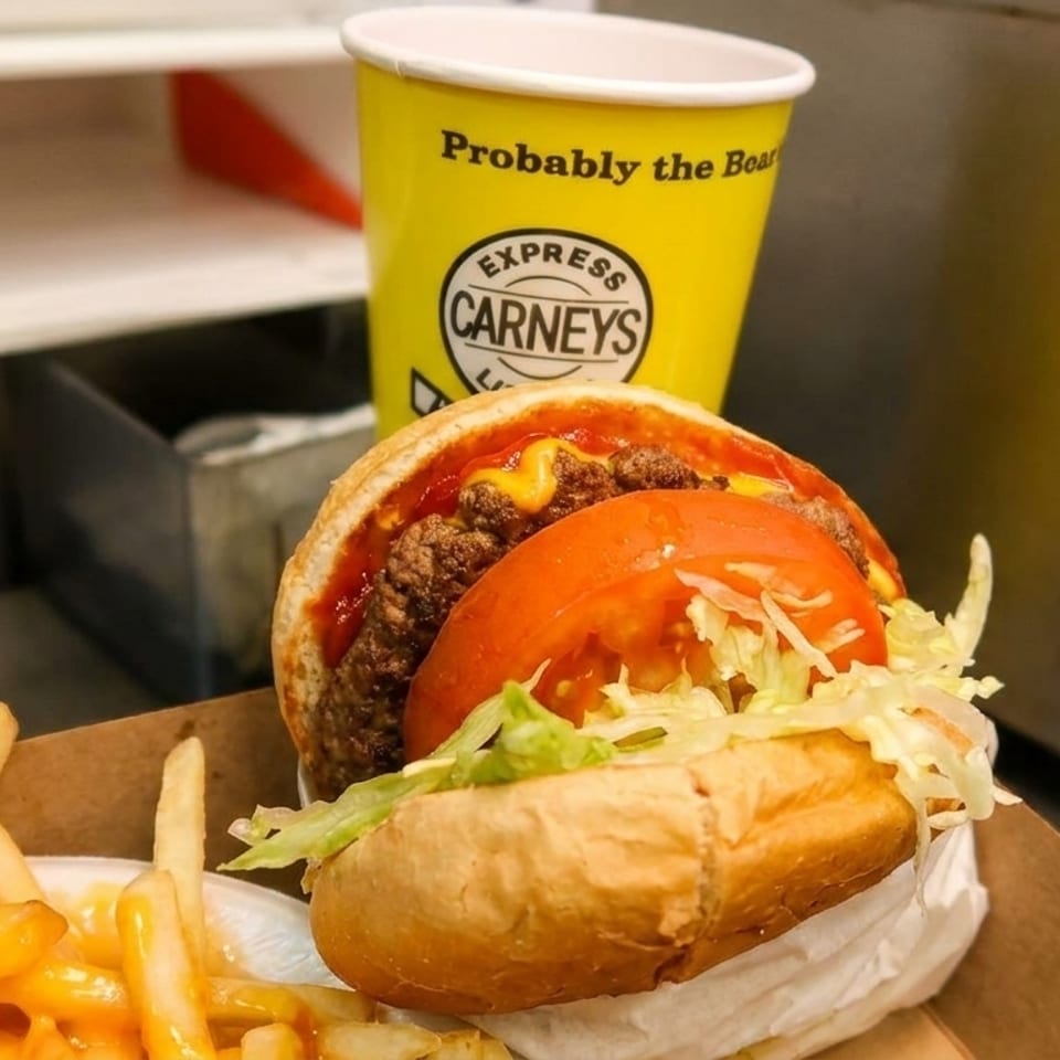 Carney's burger with tomato and lettuce, cheese fries, and a yellow Carney's cup.