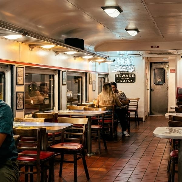 Diners seated inside a train car restaurant with a "Beware of the Trains" sign.